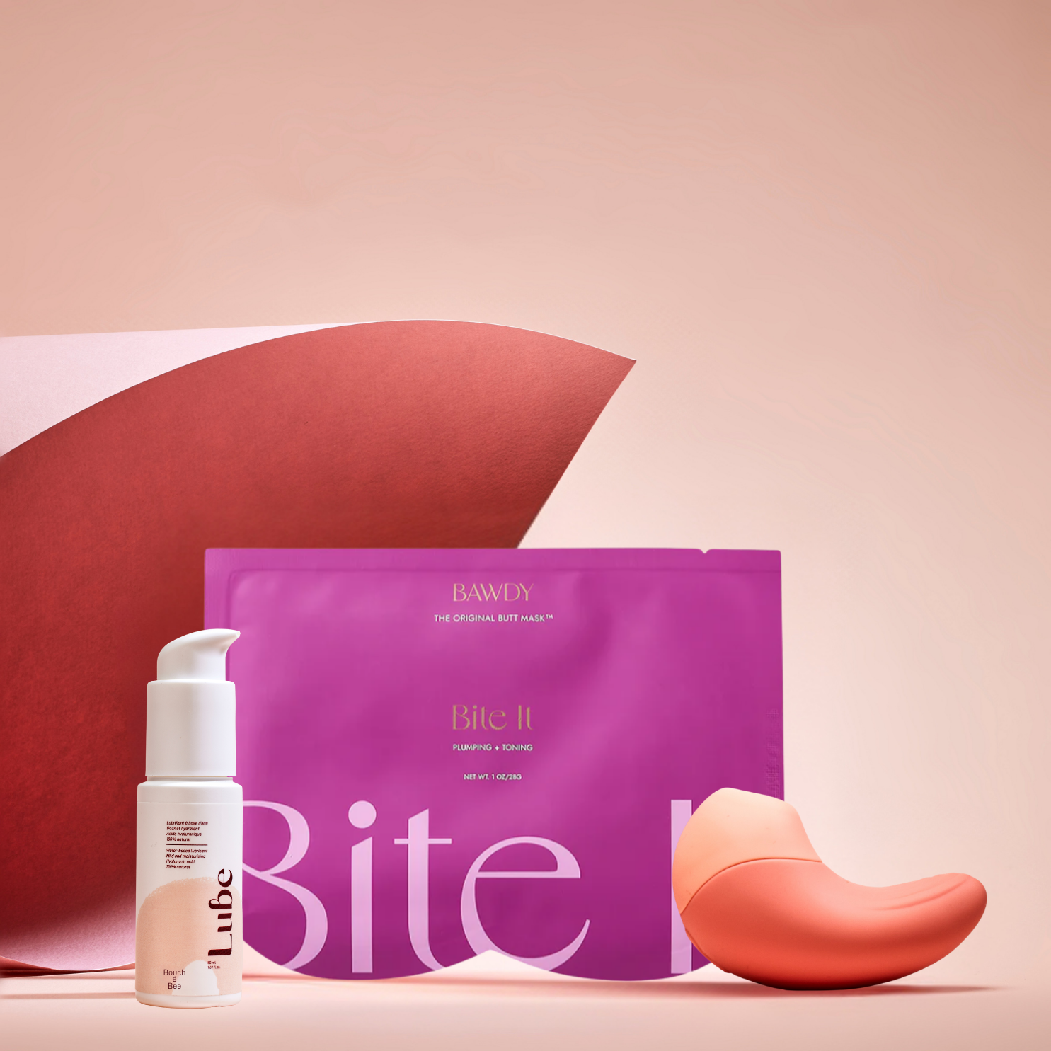 C'est une photo du coffret Badass avec Ona, stimulateur clitoridien vibrant de Bouche Bée, Lube, le lubrifiant 100% naturel à l'acide hyaluronique, le butt mask collection 4 masques de Bawdy, rose, packaging posé sur des fesses