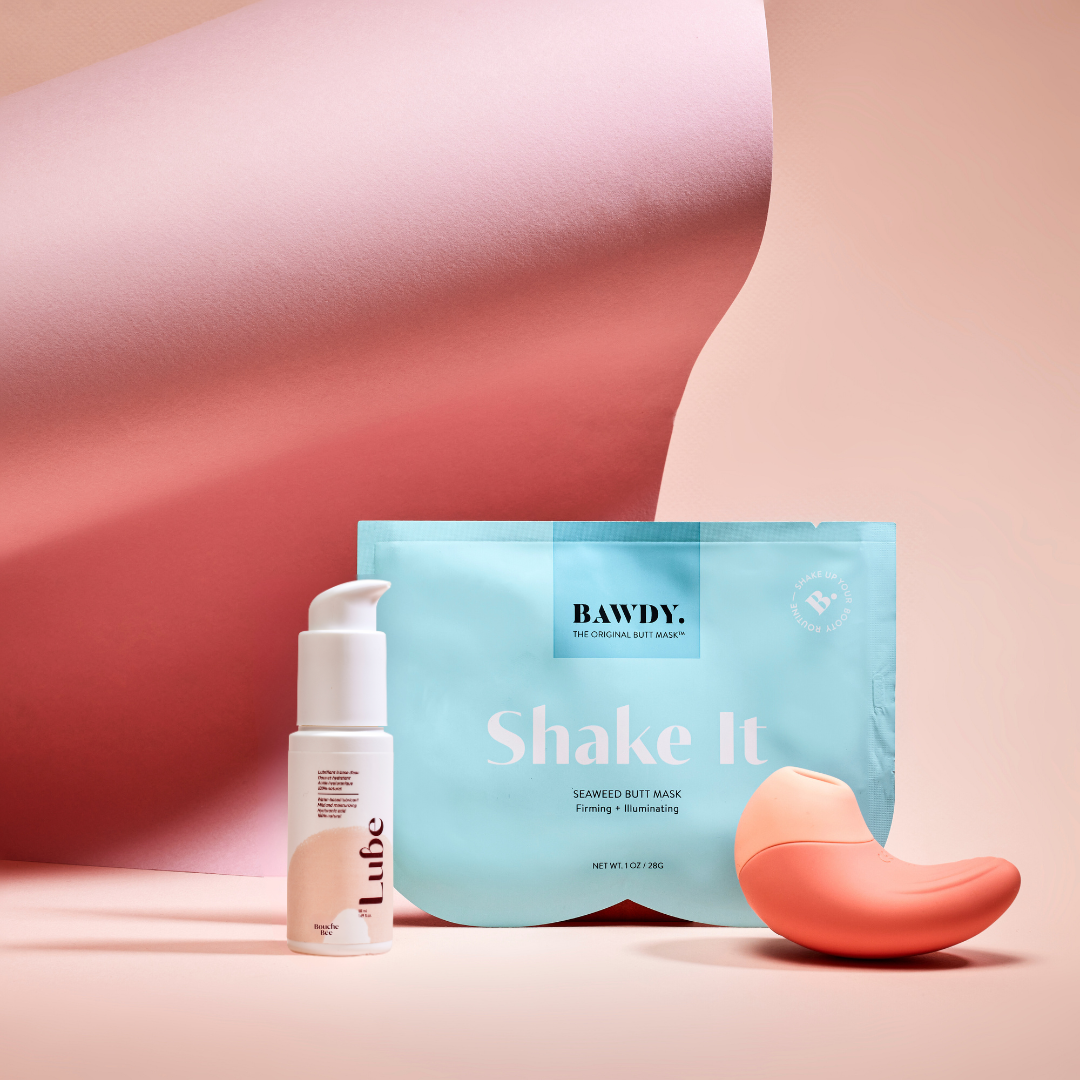 C'est une photo du coffret Badass avec Ona, stimulateur clitoridien vibrant de Bouche Bée, Lube, le lubrifiant 100% naturel à l'acide hyaluronique, le butt mask collection 4 masques de Bawdy, jaune, packaging posé sur des fesses