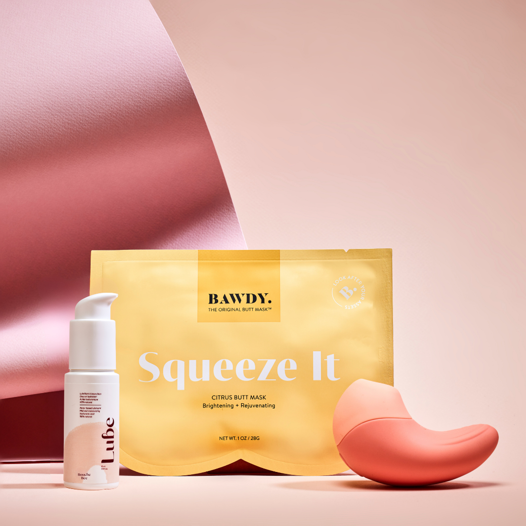 C'est une photo du coffret Badass avec Ona, stimulateur clitoridien vibrant de Bouche Bée, Lube, le lubrifiant 100% naturel à l'acide hyaluronique, le butt mask collection 4 masques de Bawdy, jaune, packaging posé sur des fesses