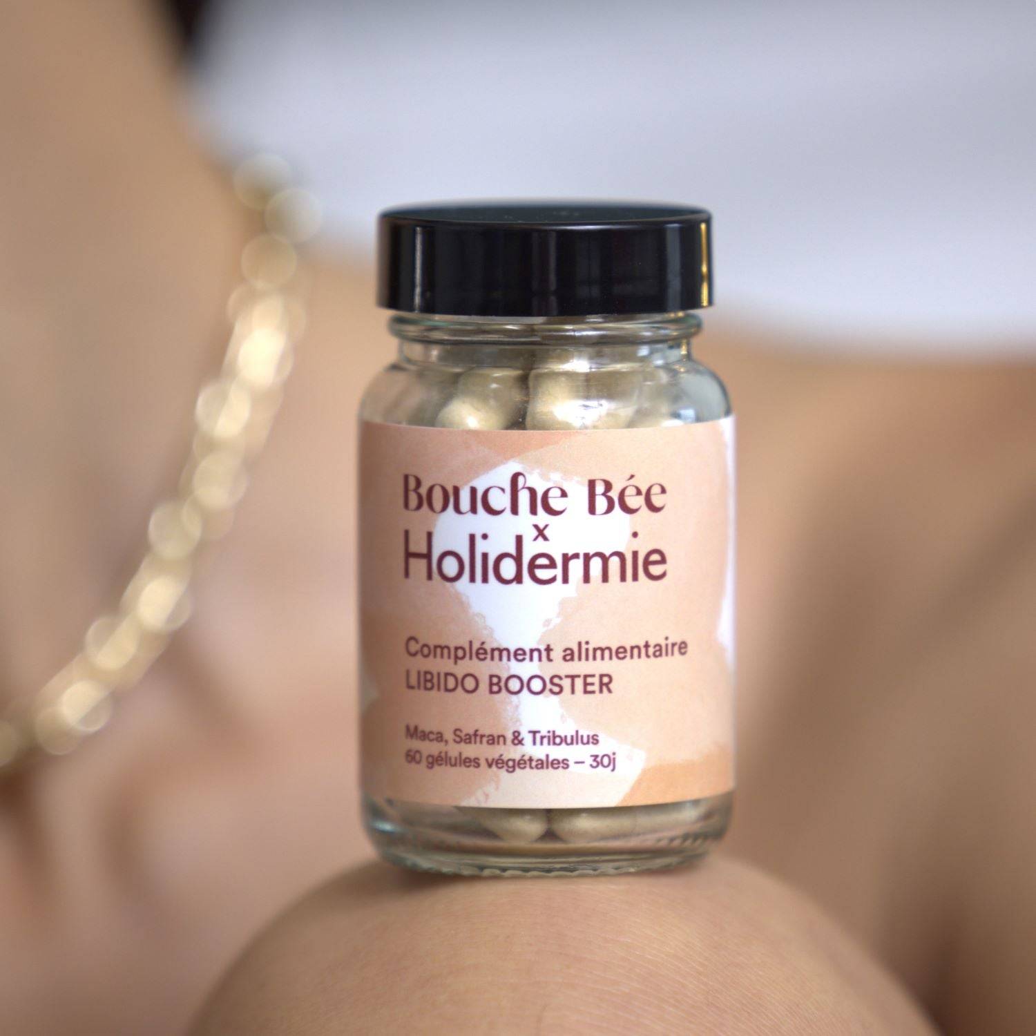 Complément alimentaire Libido Booster Bouche Bée x Holidermie en pot transparent avec capsules végétales, posé sur un genou.